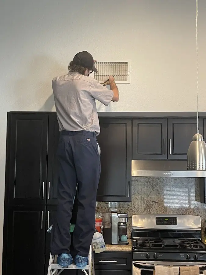 Technician inspecting an air vent during HVAC service in Oak Grove